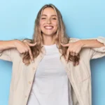 Frau, mit blonden Haaren, zeigt nach unten und lacht dabei.
